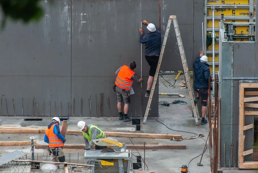 A construction worker in a hi-vis vest filling in paperwork over building plans on site