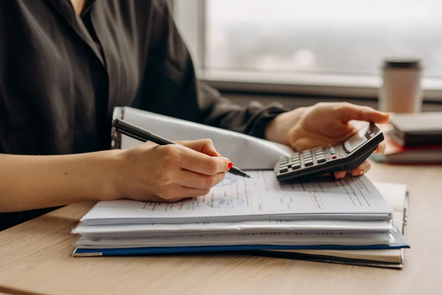 A director's hands reviewing company financial documents with a calculator at a desk A director's hands reviewing company financial documents with a calculator at a desk