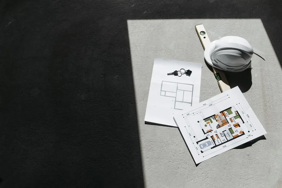 Construction project floor plans laid out beside a spirit level and hard hat, the kind of long-term contract tracked as work in progress
