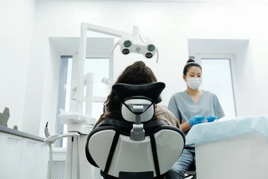 A dentist preparing instruments beside a patient in a modern UK dental practice treatment room A dentist preparing instruments beside a patient in a modern UK dental practice treatment room