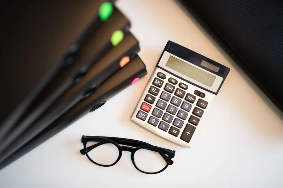 A calculator, record folders and reading glasses laid out to work out the tax due on an eBay business account A calculator, record folders and reading glasses laid out to work out the tax due on an eBay business account