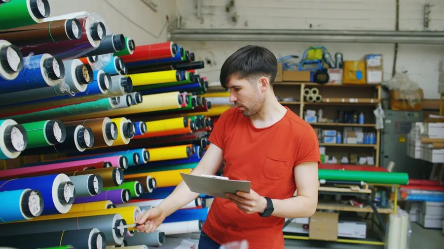 A small online marketplace seller checking stock levels against records on a clipboard in their workshop A small online marketplace seller checking stock levels against records on a clipboard in their workshop