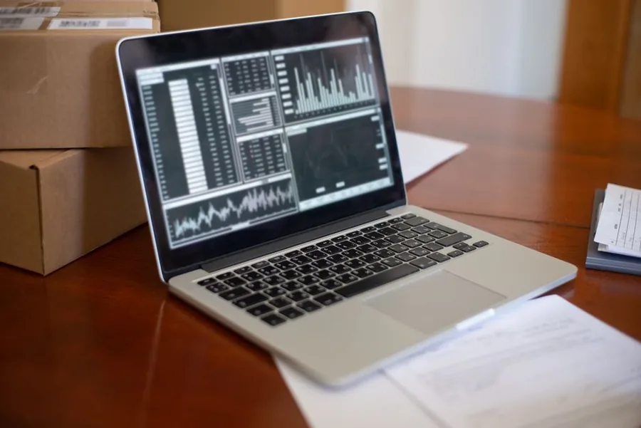 A laptop showing sales and payment analytics beside parcels ready to post, as an eBay seller reconciles managed payments payouts