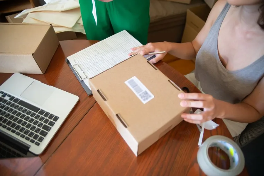 A sole trader packing an eBay parcel beside a laptop and a paper ledger while totting up year-end figures A sole trader packing an eBay parcel beside a laptop and a paper ledger while totting up year-end figures