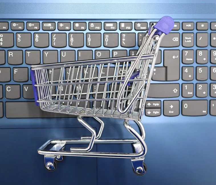 A miniature shopping trolley resting on a laptop keyboard, representing an online store's sales and performance data A miniature shopping trolley resting on a laptop keyboard, representing an online store's sales and performance data