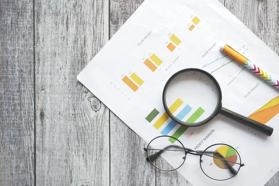 Printed profit margin charts and a magnifying glass on a desk, the detail an ecommerce seller checks to find their true net margin Printed profit margin charts and a magnifying glass on a desk, the detail an ecommerce seller checks to find their true net margin