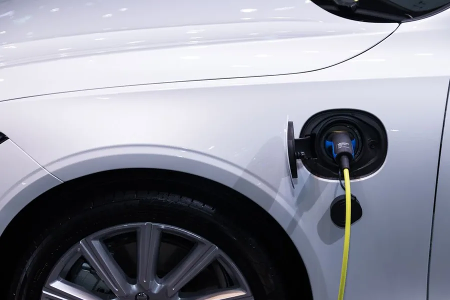 A white electric company car plugged in to charge, its cable connected to the side charging port A white electric company car plugged in to charge, its cable connected to the side charging port