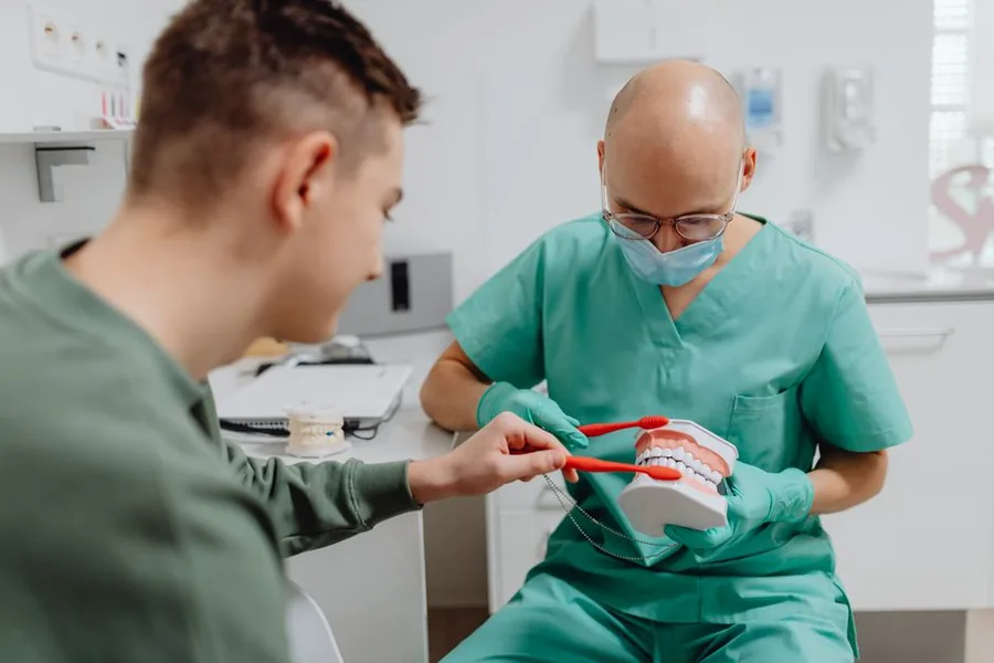 A dentist in scrubs explaining oral care to a patient during a UK dental practice appointment A dentist in scrubs explaining oral care to a patient during a UK dental practice appointment