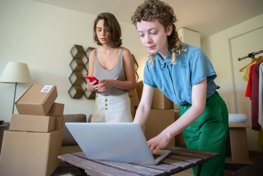 Small online retailers checking orders on a laptop beside stacked parcels in a home packing space Small online retailers checking orders on a laptop beside stacked parcels in a home packing space