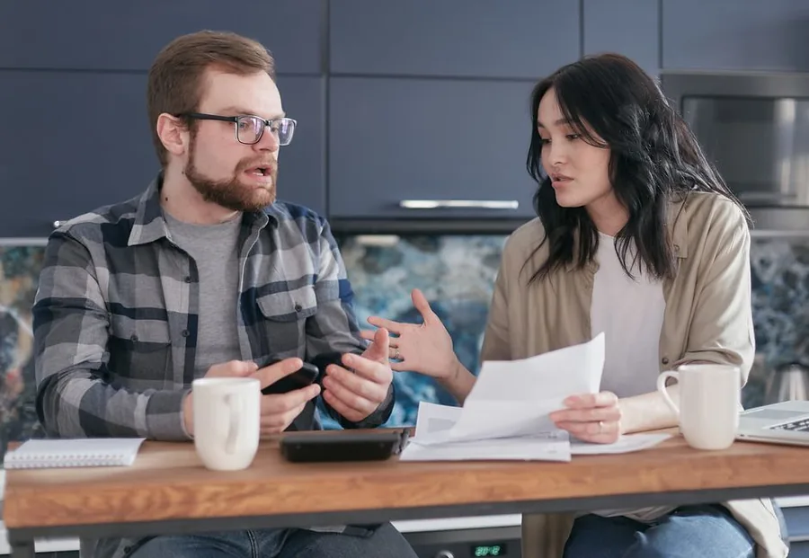 A married couple reviewing rental property paperwork together at their kitchen table, weighing up how to divide the income A married couple reviewing rental property paperwork together at their kitchen table, weighing up how to divide the income