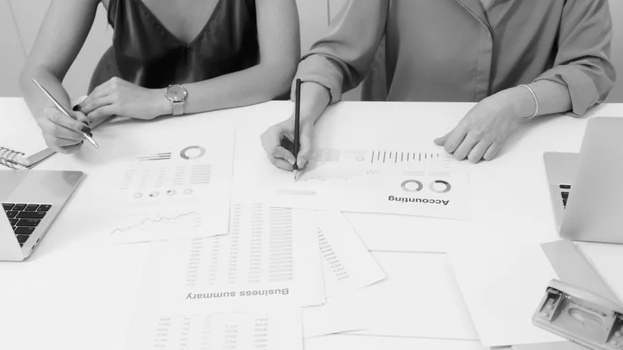 A UK business owner and accountant reviewing financial statements, charts and a business summary report across a shared desk A UK business owner and accountant reviewing financial statements, charts and a business summary report across a shared desk