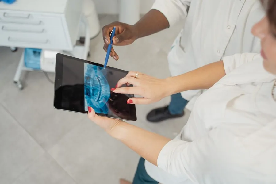 A dental professional reviewing a patient X-ray on a tablet in a UK practice, weighing the running costs behind each treatment A dental professional reviewing a patient X-ray on a tablet in a UK practice, weighing the running costs behind each treatment