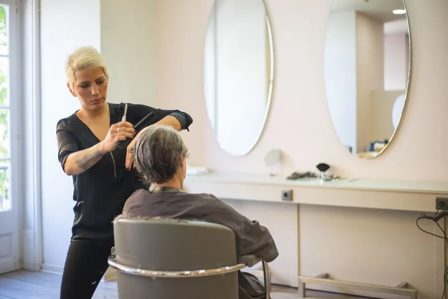 A self-employed hairdresser trimming a client's hair at a rented salon chair, the kind of stylist tracking tips and expenses A self-employed hairdresser trimming a client's hair at a rented salon chair, the kind of stylist tracking tips and expenses