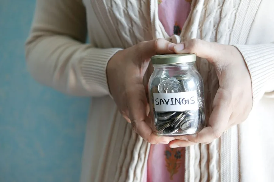 A saver holding a glass jar of coins labelled Savings, weighing up how HMRC taxes interest on their account A saver holding a glass jar of coins labelled Savings, weighing up how HMRC taxes interest on their account