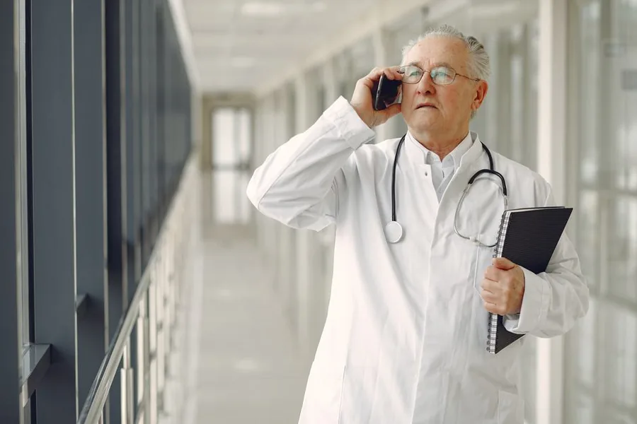 A hospital doctor on a ward corridor taking a call between shifts, the kind of locum work that shapes NHS pension and tax A hospital doctor on a ward corridor taking a call between shifts, the kind of locum work that shapes NHS pension and tax