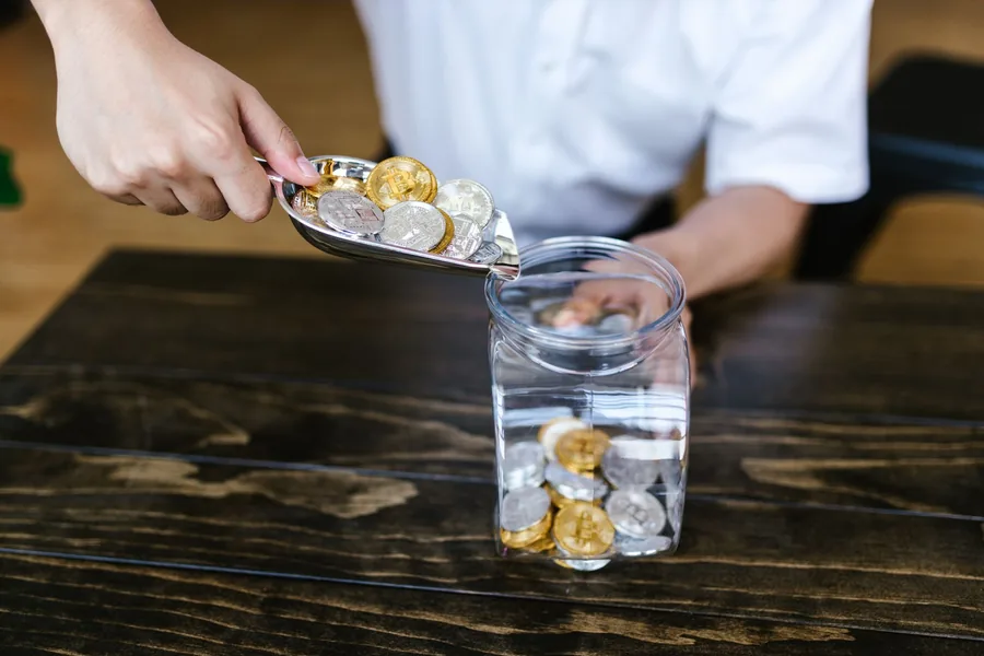 Coins being tipped into a glass savings jar, illustrating a sole trader putting money aside from each payment for tax Coins being tipped into a glass savings jar, illustrating a sole trader putting money aside from each payment for tax