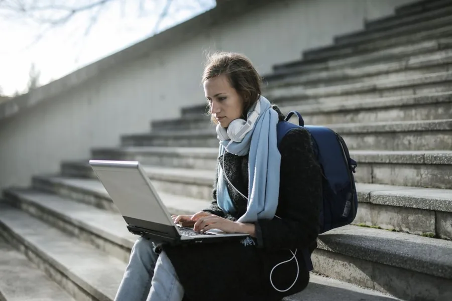 A student sitting on campus steps with a laptop, the kind of graduate who later repays their loan automatically through payroll A student sitting on campus steps with a laptop, the kind of graduate who later repays their loan automatically through payroll