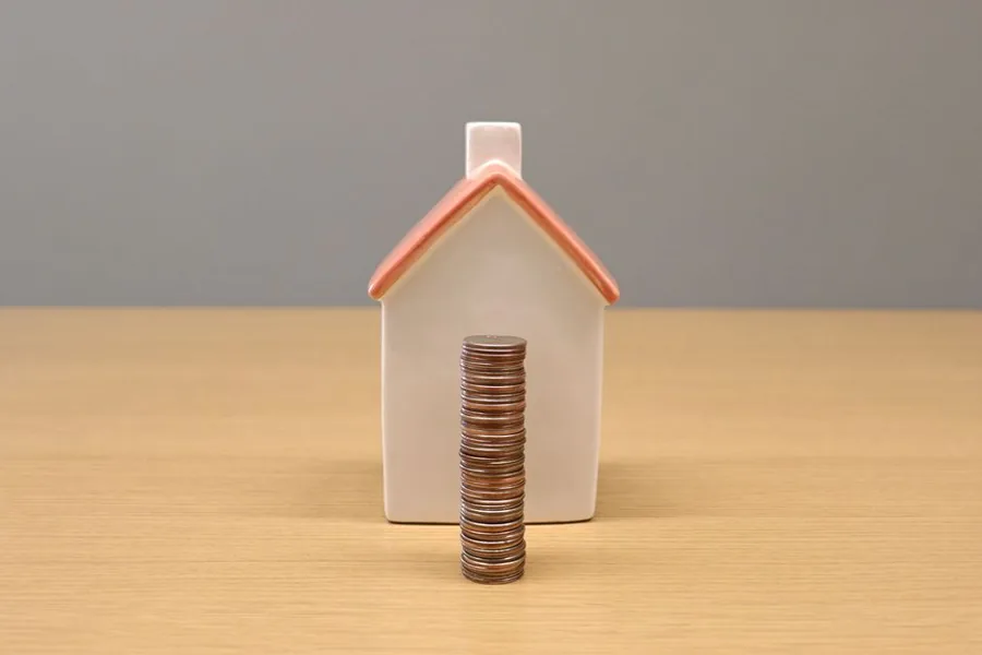 A model house beside a stack of coins, representing the value built up in a UK property and the tax due when it is sold A model house beside a stack of coins, representing the value built up in a UK property and the tax due when it is sold