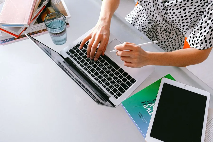 A freelance accountant working at a laptop, making notes on a tablet while reviewing figures at a home desk A freelance accountant working at a laptop, making notes on a tablet while reviewing figures at a home desk