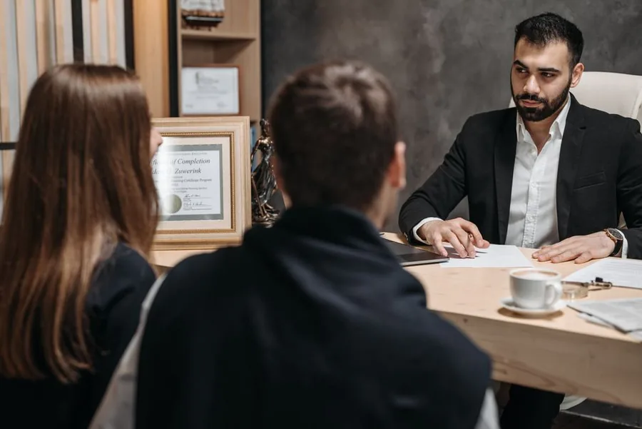 A couple reviewing their tax position with an accountant across a desk while sorting out an emergency tax refund claim A couple reviewing their tax position with an accountant across a desk while sorting out an emergency tax refund claim