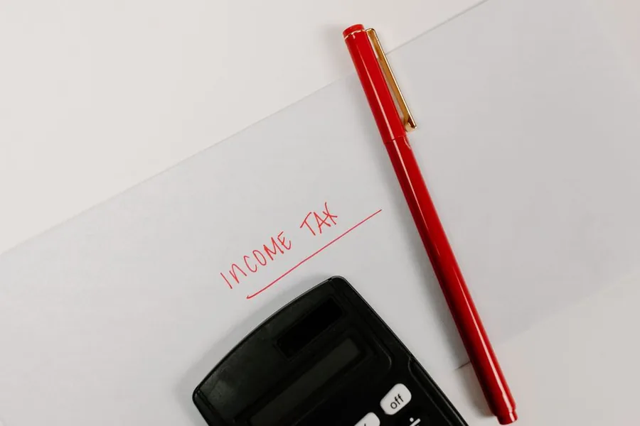 Income tax written in red beside a calculator, the kind of paperwork where your UK tax reference number is printed Income tax written in red beside a calculator, the kind of paperwork where your UK tax reference number is printed