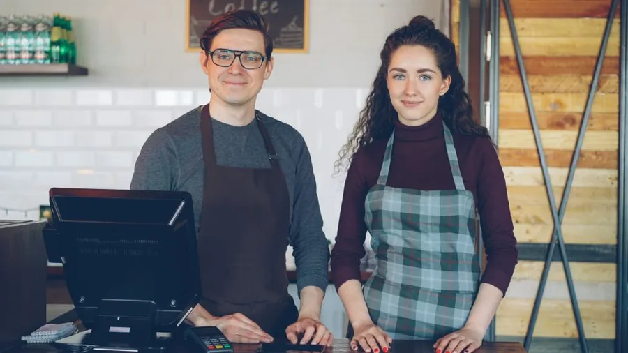 Two business partners standing together behind the counter of their cafe, running the venture jointly