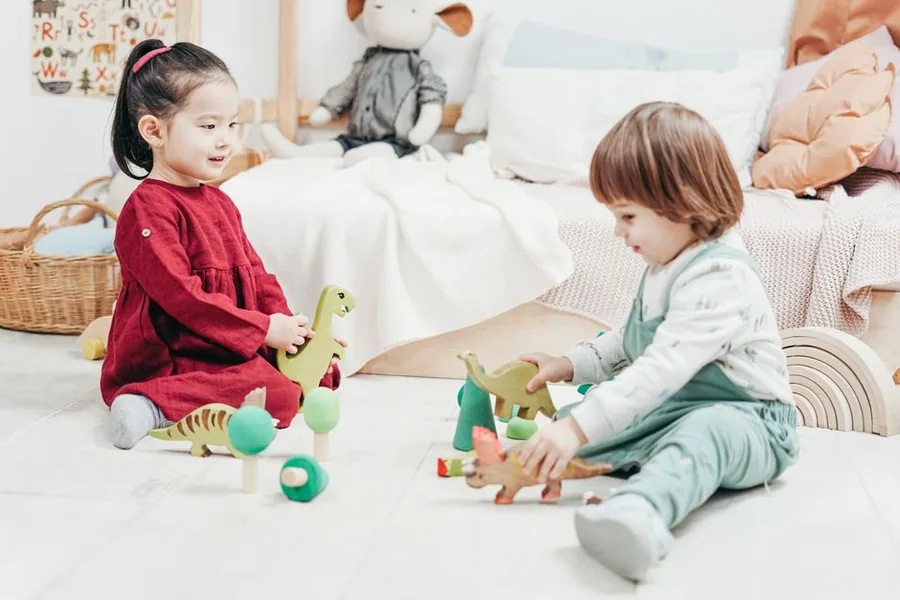 A childminder playing with a young child on the floor of a toy-filled playroom A childminder playing with a young child on the floor of a toy-filled playroom