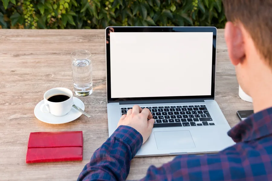 A self-employed worker at a laptop with a coffee, working out the taxable profit figure for their Self Assessment tax return