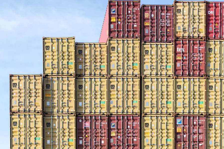Stacked shipping containers at a UK port, the imported goods that trigger import VAT and postponed VAT accounting for Amazon FBA sellers Stacked shipping containers at a UK port, the imported goods that trigger import VAT and postponed VAT accounting for Amazon FBA sellers