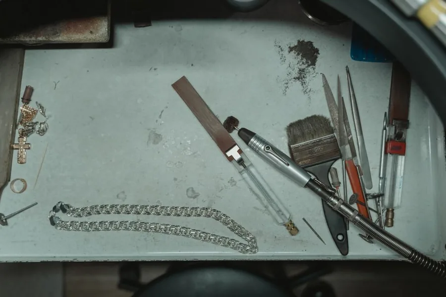 Overhead view of a jeweller's workbench with hand tools and a silver chain in a small UK workshop