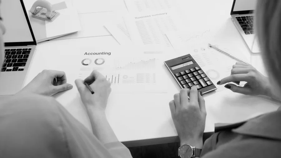 Two colleagues reviewing company accounts and financial summaries with a calculator ahead of a filing deadline