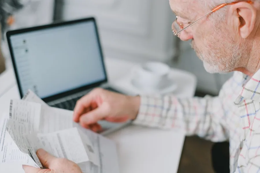 A locum GP reviewing pension contribution statements and NHS paperwork at a laptop to check the tier their annualised income falls into A locum GP reviewing pension contribution statements and NHS paperwork at a laptop to check the tier their annualised income falls into