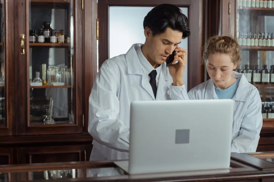 A locum pharmacist working on a laptop at the dispensary counter, reviewing self assessment paperwork A locum pharmacist working on a laptop at the dispensary counter, reviewing self assessment paperwork