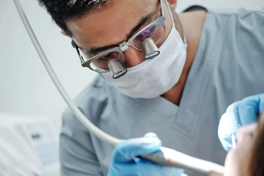 A dentist wearing magnifying loupes while treating a patient, the kind of clinical kit that can be a tax deductible expense A dentist wearing magnifying loupes while treating a patient, the kind of clinical kit that can be a tax deductible expense