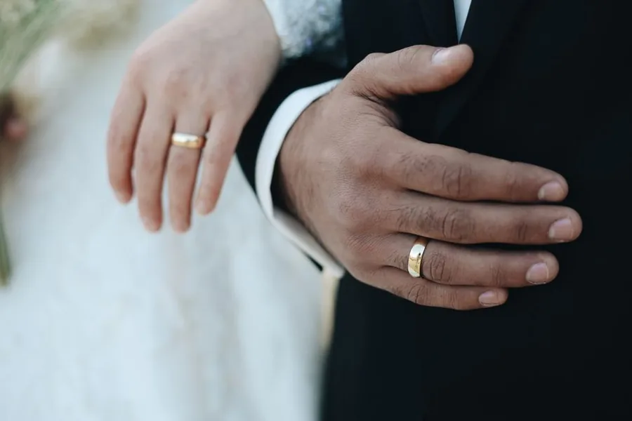 A married couple clasping hands, both wearing wedding rings, the marital status that qualifies for Marriage Allowance