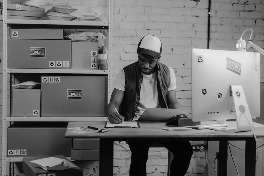 An online marketplace seller working through paperwork at a desk surrounded by parcels ready to post An online marketplace seller working through paperwork at a desk surrounded by parcels ready to post