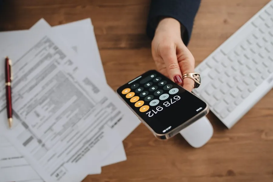 A landlord tallying rental figures on a phone beside a keyboard and paperwork while keeping digital tax records A landlord tallying rental figures on a phone beside a keyboard and paperwork while keeping digital tax records