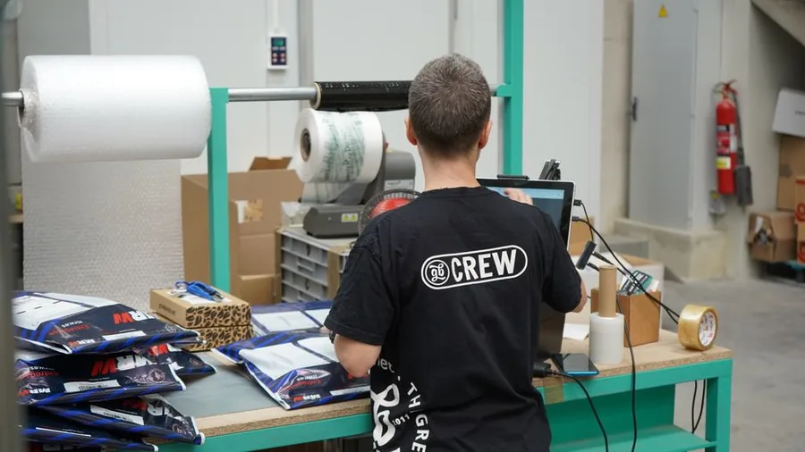 A UK online reseller packing branded mailers at a despatch station while checking orders on screen