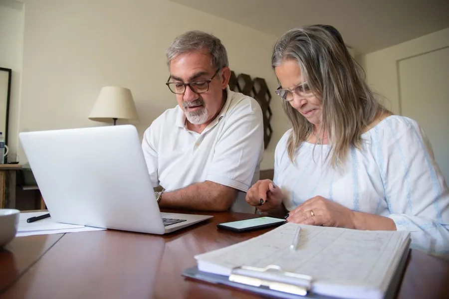 A retired couple reviewing their pension paperwork and finances at home with a laptop A retired couple reviewing their pension paperwork and finances at home with a laptop