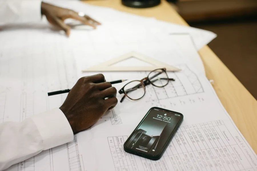 A construction contractor at a desk checking their phone against project paperwork before filing a CIS return