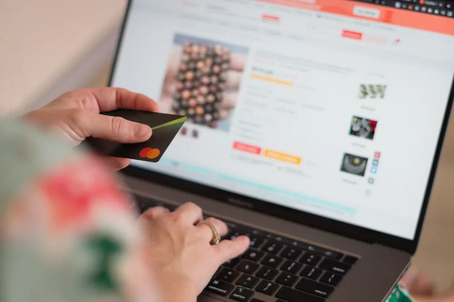 A shopper browsing an online marketplace listing on a laptop while holding a payment card to complete a purchase A shopper browsing an online marketplace listing on a laptop while holding a payment card to complete a purchase