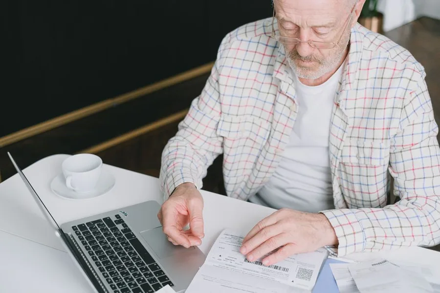 An older man at his laptop reviewing paperwork as he works out pension contributions and the income tax relief he can claim An older man at his laptop reviewing paperwork as he works out pension contributions and the income tax relief he can claim