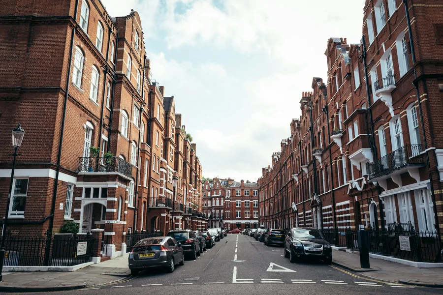 A London street of red brick mansion blocks with cars parked along both kerbs, typical of the flats many landlords let