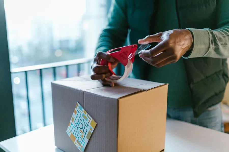 An online marketplace seller taping up a customer parcel before dispatch from a home workspace An online marketplace seller taping up a customer parcel before dispatch from a home workspace