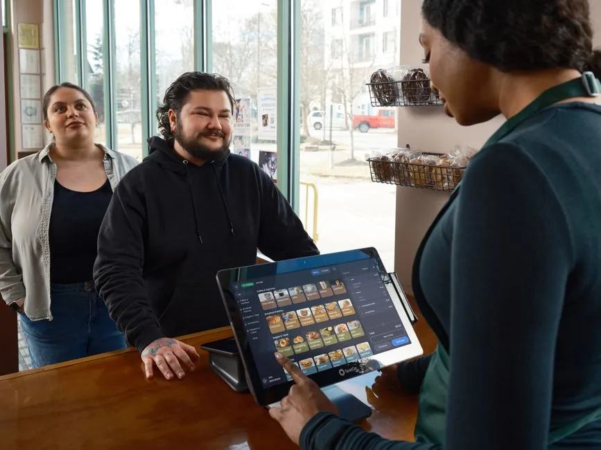 A small business owner taking a customer order on a tablet till, the kind of sole trader who needs to register as self-employed with HMRC A small business owner taking a customer order on a tablet till, the kind of sole trader who needs to register as self-employed with HMRC