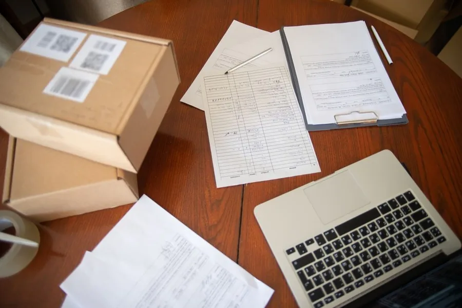 A UK eBay seller packing parcels and working through fee paperwork on a laptop at the despatch desk A UK eBay seller packing parcels and working through fee paperwork on a laptop at the despatch desk