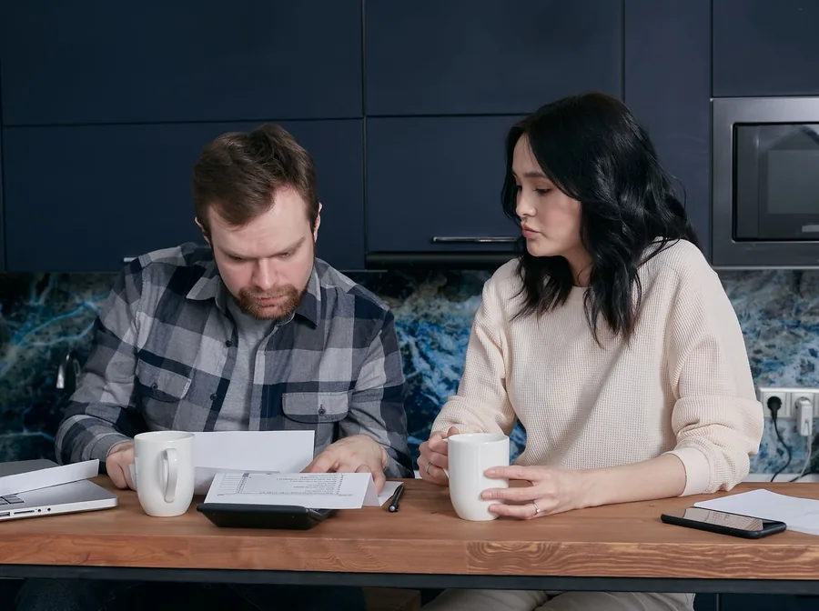 Couple at a kitchen table checking a printed pay statement together, using a calculator to work out their monthly take-home pay