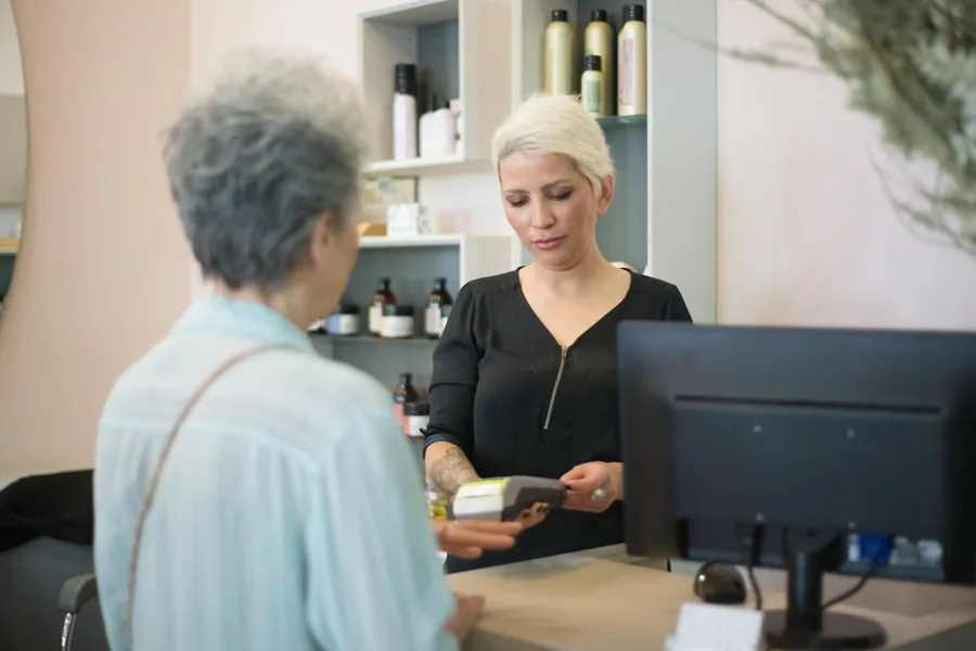 A stylist at a UK salon reception taking a client's card payment at the till, where gift voucher VAT is accounted for A stylist at a UK salon reception taking a client's card payment at the till, where gift voucher VAT is accounted for