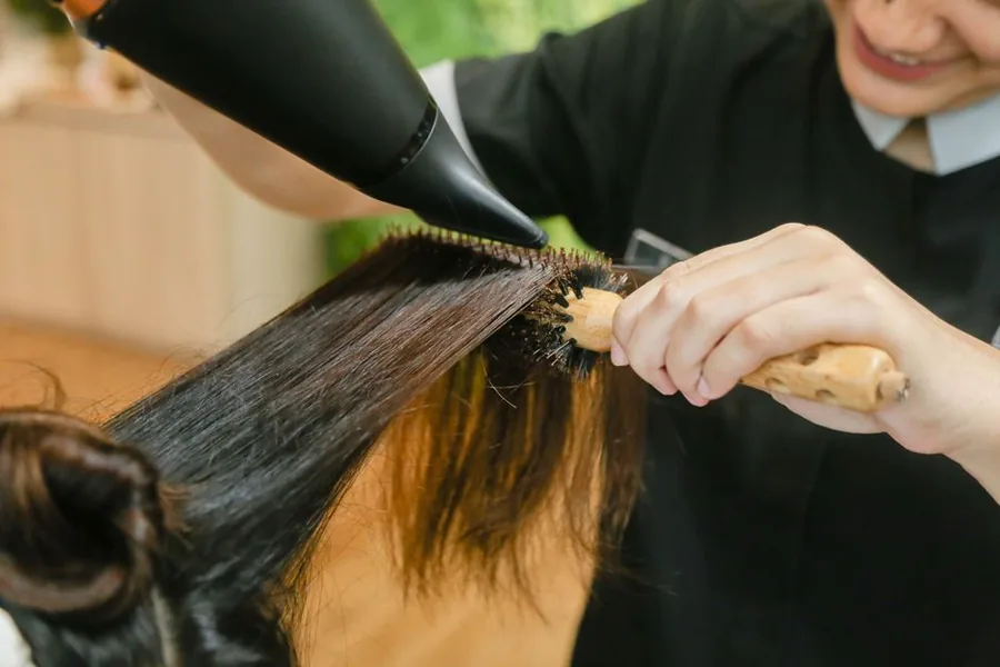 A salon stylist blow-drying a client's hair, the front-line service work now covered by the Tipping Act 2023 tronc rules A salon stylist blow-drying a client's hair, the front-line service work now covered by the Tipping Act 2023 tronc rules