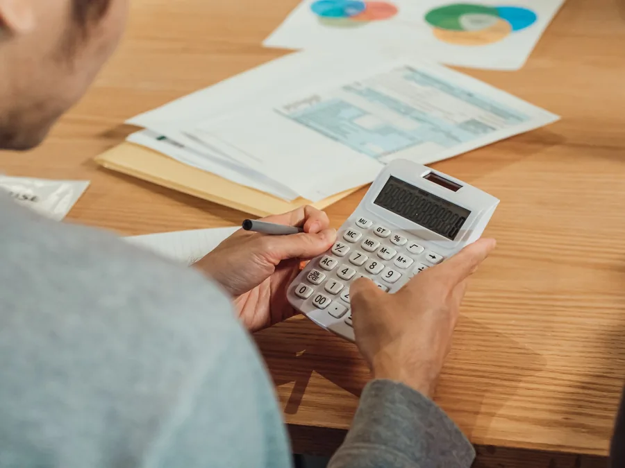 A person using a calculator to work through income tax figures beside financial paperwork at a desk